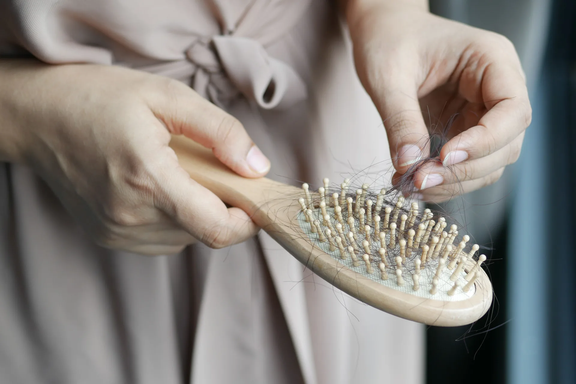 Hands gently removing loose strands of hair from a wooden hairbrush